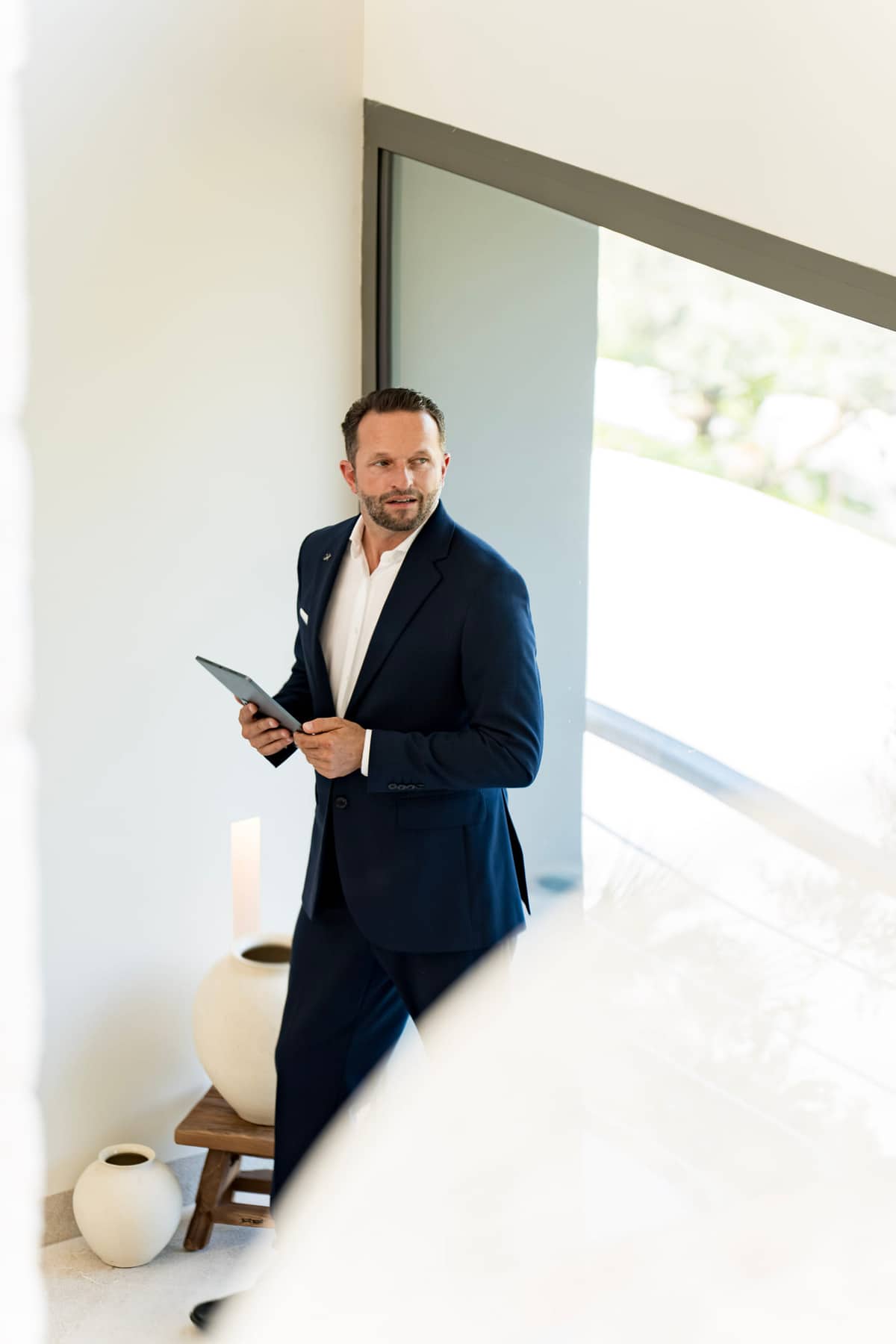 Daniel Rudolf, Gründer der Xclusive Butler School, im marineblauen Anzug mit Tablet beim Management einer modernen Luxusvilla.